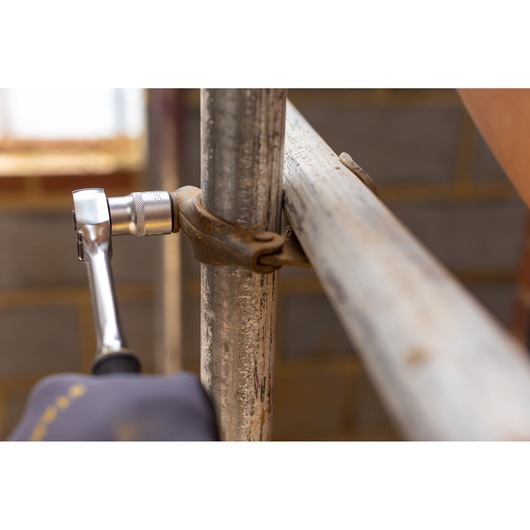 STANLEY FMMT17229-0 ratchet wrench tightening metal clamp on scaffold pipe, close-up photography.