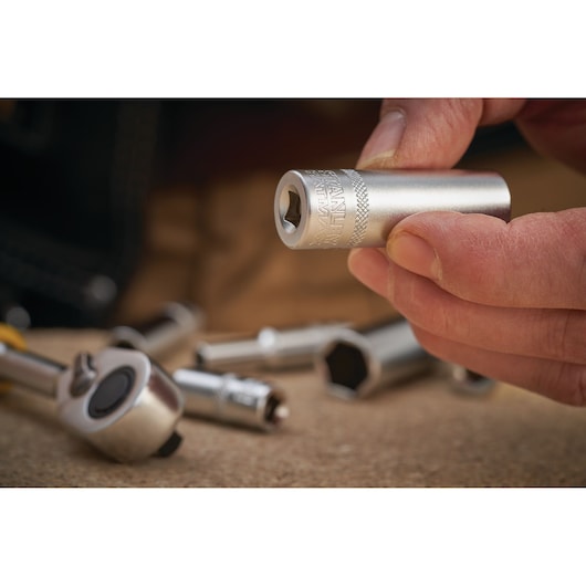 STANLEY FMMT17963-0 chrome socket held in hand, with ratchet and other sockets in background, close-up photo.