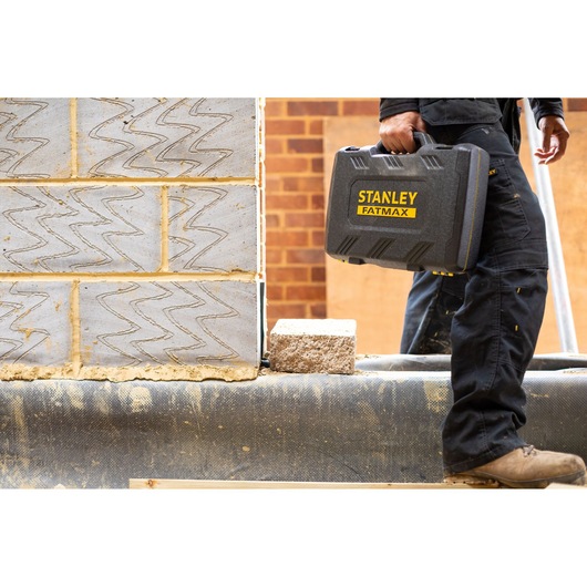 Photo of STANLEY FMMT82683-0 tool case in worker’s hand at construction site, with brick background.