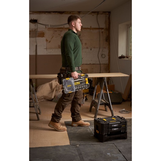 Photo of a worker holding a STANLEY FMMT98104-0 socket set in a transparent case, standing in a workshop.