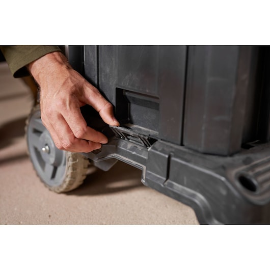 STANLEY FMST1-72363 tool box close-up showing hand opening the latch near wheel, photography.