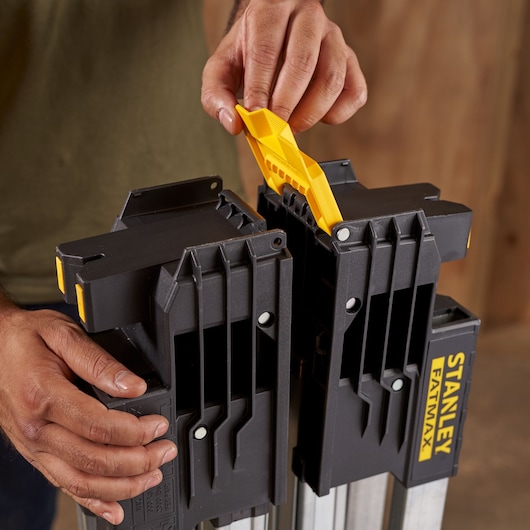 STANLEY FMST1-75763 sawhorse close-up, person adjusting yellow handle, black body with yellow accents.