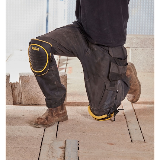 STANLEY FMST82961-1 knee pads worn on work pants at a construction site, black with yellow trim.