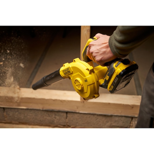 Stanley SFMCBL01B cordless blower in use, yellow and black, close-up side angle, clearing sawdust.