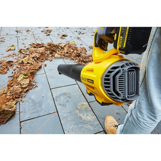 STANLEY SFMCBL7B leaf blower on patio, yellow and black design, photographed in use clearing dry leaves.