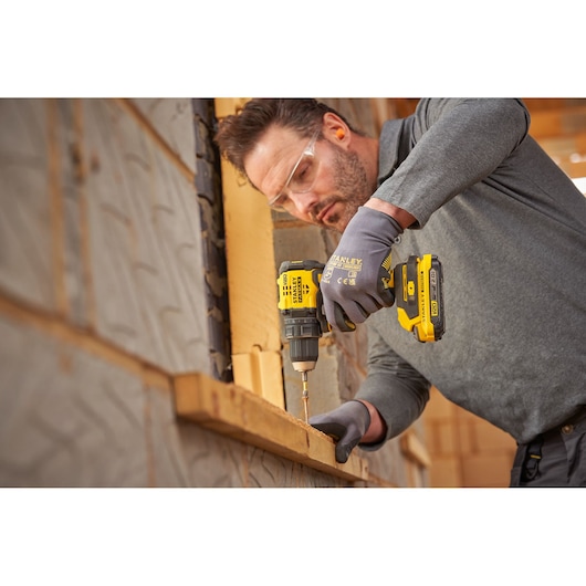 Photo of a person using a STANLEY SFMCD714B-XJ cordless drill, driving a screw into wood at a construction site.