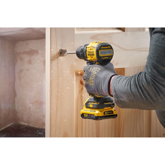 Photo of STANLEY SFMCD714D2T cordless drill in use drilling into wood, yellow and black design, close-up view.