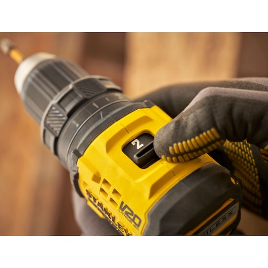 Photo of STANLEY SFMCD714D2T drill close-up, gloved hand adjusting speed setting, yellow and black body.