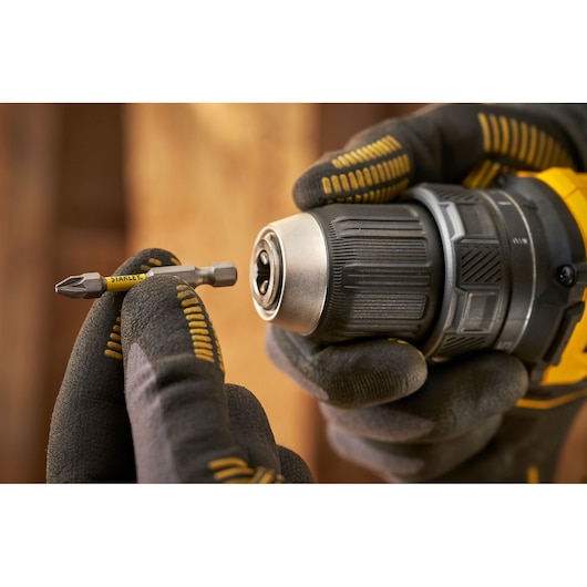 STANLEY SFMCD714D2T cordless drill held with gloved hands and a STANLEY screwdriver bit, angled close-up.
