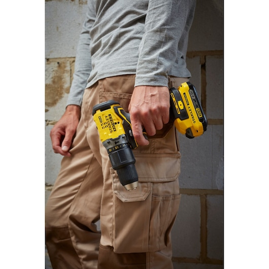STANLEY SFMCD715C2K cordless drill held by person in work pants, outdoor setting.