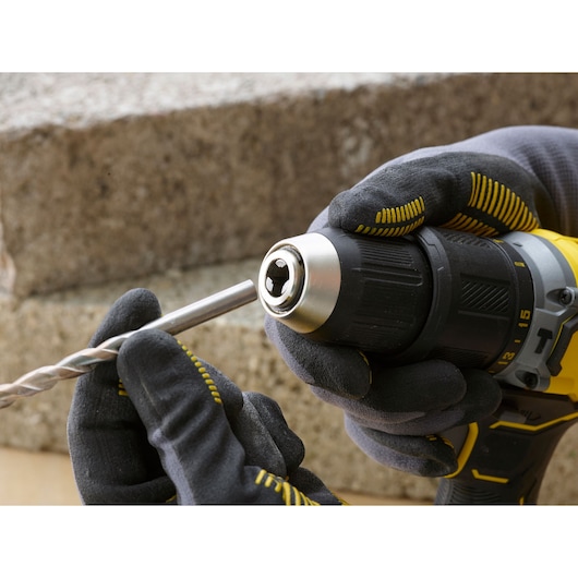 STANLEY SFMCD715D1K cordless drill being fitted with a drill bit, close-up view with gloved hands.