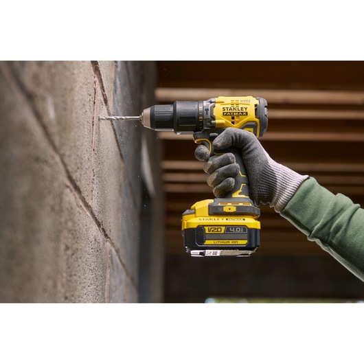 STANLEY SFMCD715M2K cordless drill being used to drill into a concrete wall, side view with gloved hand.