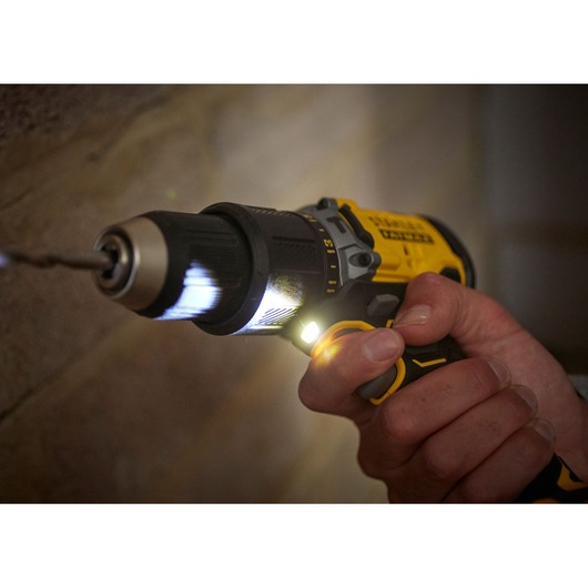 STANLEY SFMCD715M2K cordless drill in use, yellow and black, close-up with LED light on.