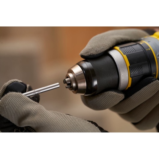 Photo of STANLEY SFMCD721B cordless drill being fitted with a metal bit, close-up, gloves visible.