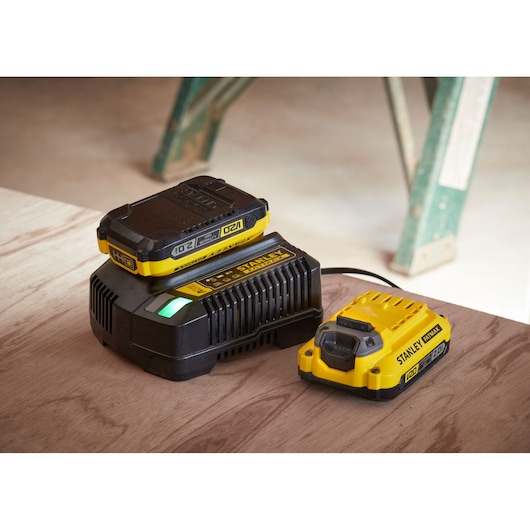 STANLEY SFMCD721M2K battery charger and spare battery, yellow and black, angled view on wooden surface.