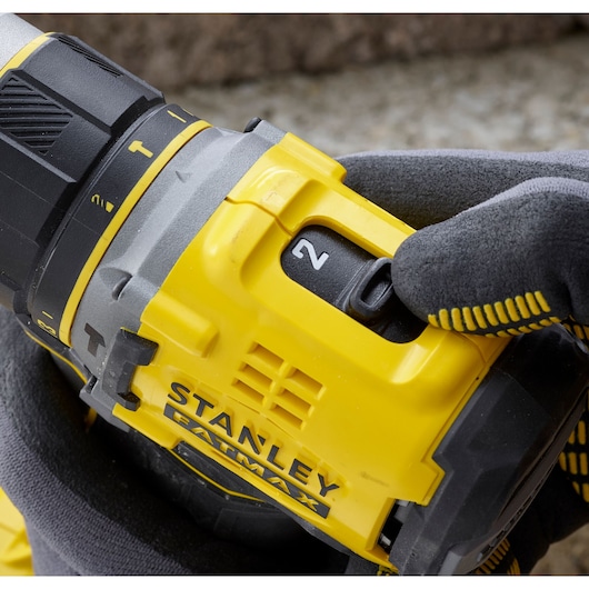 STANLEY SFMCD721M2K cordless drill close-up, yellow and black, showing speed selector, gloved hand.