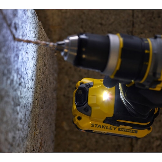 STANLEY SFMCD721M2K cordless drill with LED light drilling into concrete wall, close-up photography.
