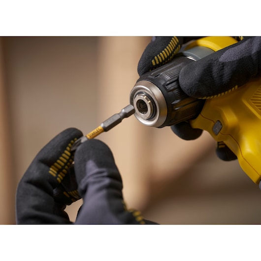 STANLEY SFMCD750D2K drill in use, close-up of bit being inserted, worker wearing black gloves.