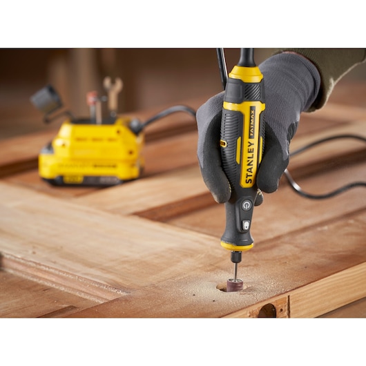 STANLEY SFMCE030B rotary tool used for sanding wood, close-up view of tool in hand on work surface.
