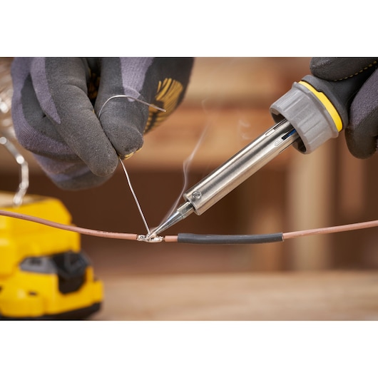 STANLEY SFMCE040B soldering iron in use, close-up, joining wires with solder, gloved hands visible.