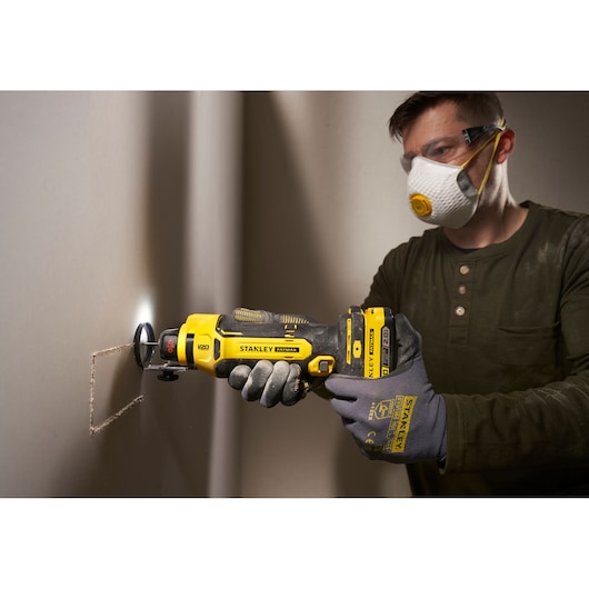 Photo of STANLEY SFMCE200B rotary tool cutting drywall, tool held by gloved hands, jobsite setting.