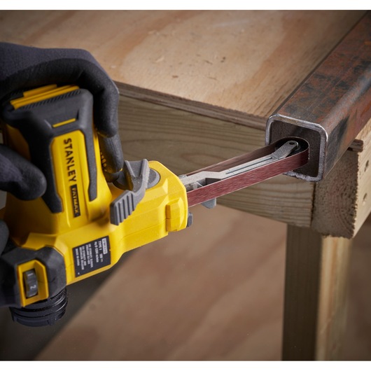 Photo of STANLEY SFMCE210D2 cordless belt file sander grinding inside a metal tube, close-up view.