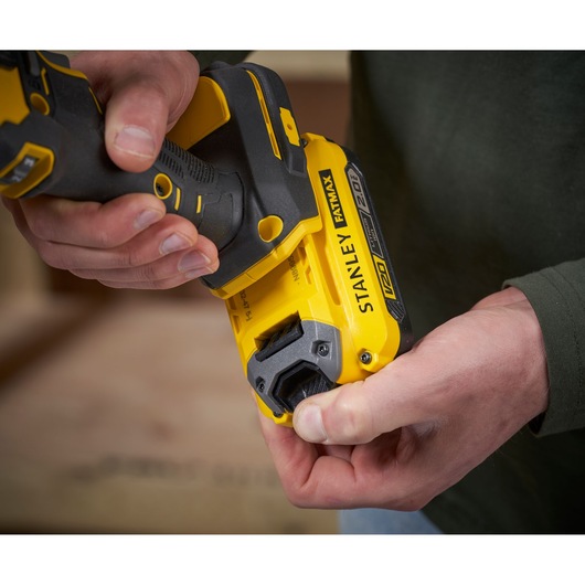 Stanley SFMCE210D2 cordless drill close-up, yellow and black, held in hand, side angle.