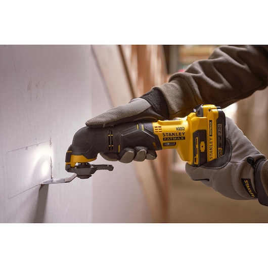 Photo of STANLEY SFMCE500B oscillating multi-tool cutting drywall, worker wearing gloves.