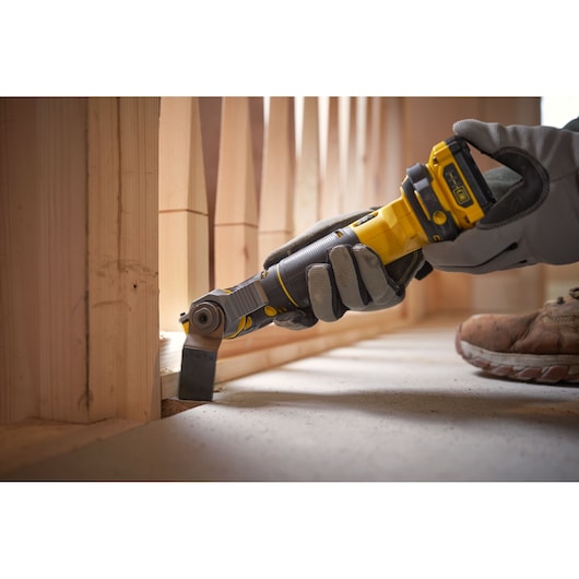 STANLEY SFMCE500D2K oscillating multi-tool in use trimming wood at floor level, close-up view.