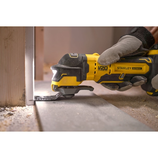 STANLEY SFMCE510B multi-tool cutting close to wall, yellow-black, side angle, construction setting.