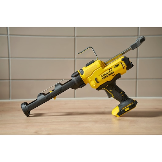 Stanley SFMCE600B cordless caulking gun, side angle, yellow and black, on wooden surface.