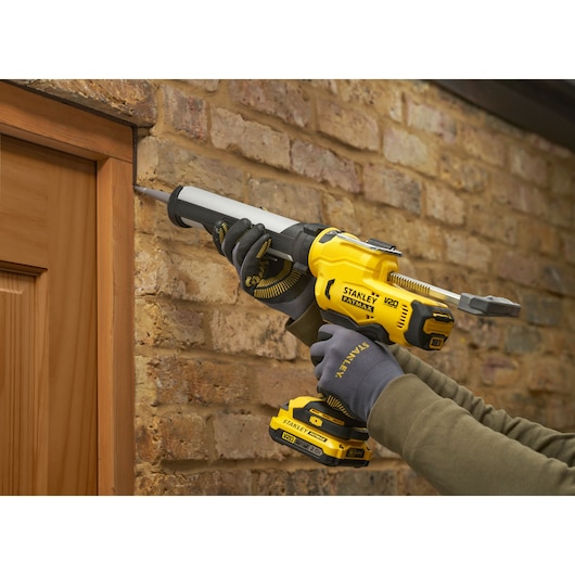 STANLEY SFMCE600B caulk gun used to seal around a wooden door frame against a brick wall.