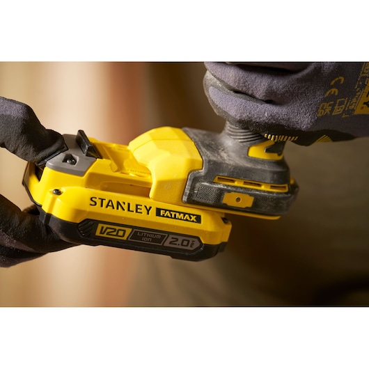 Photo of STANLEY SFMCF910B cordless impact driver with V20 2.0Ah lithium-ion battery held by gloved hand.