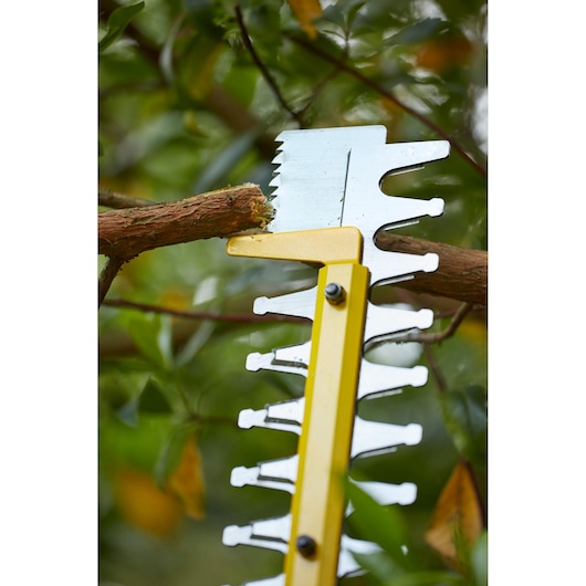 STANLEY SFMCHT855B hedge trimmer cutting a tree branch, close-up with yellow blade in outdoor setting.