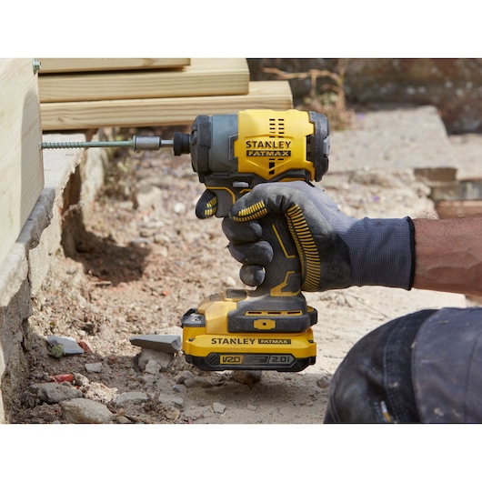 Stanley SFMCK461D2S cordless impact driver used outdoors with gloved hand, drilling into wood.