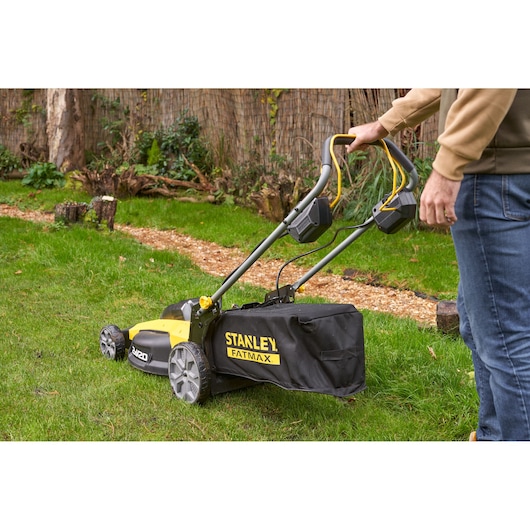 Stanley SFMCMWS251B lawn mower with grass collection bag in outdoor garden setting, side angle.