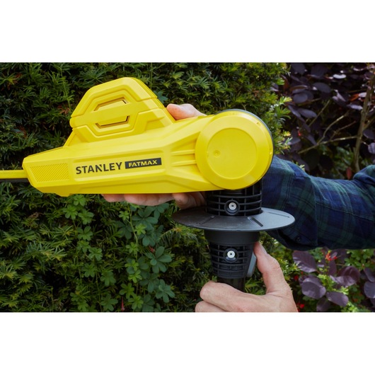STANLEY SFMCPH845B yellow hedge trimmer side view in use, close-up with hand on handle outdoors.