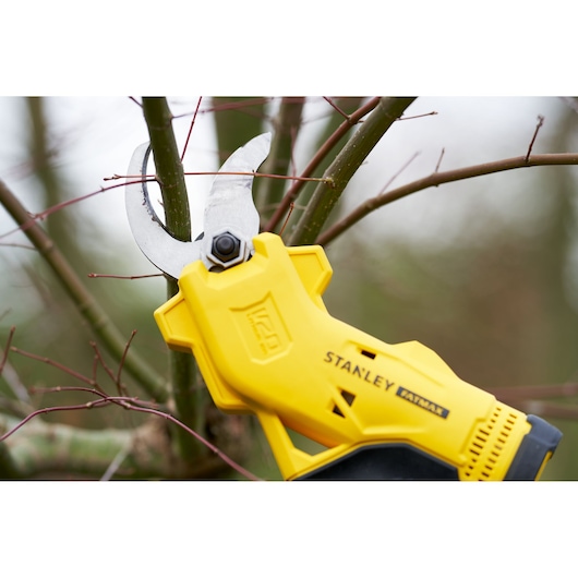STANLEY SFMCPP32B yellow cordless pruning shear cutting a tree branch outdoors, close-up.