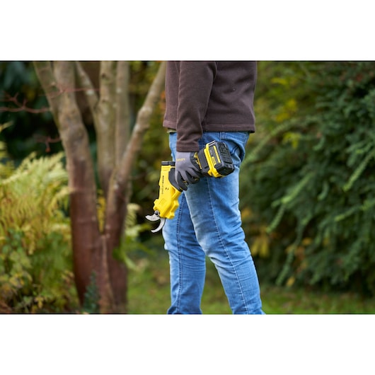 STANLEY SFMCPP32B photography of person holding yellow cordless pruning shears outdoors.