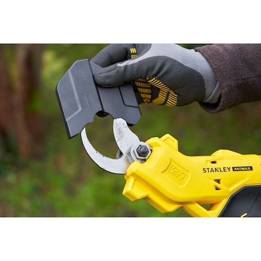 Photo of STANLEY SFMCPP32M1 yellow pruner, gloved hand placing blade cover outdoors.