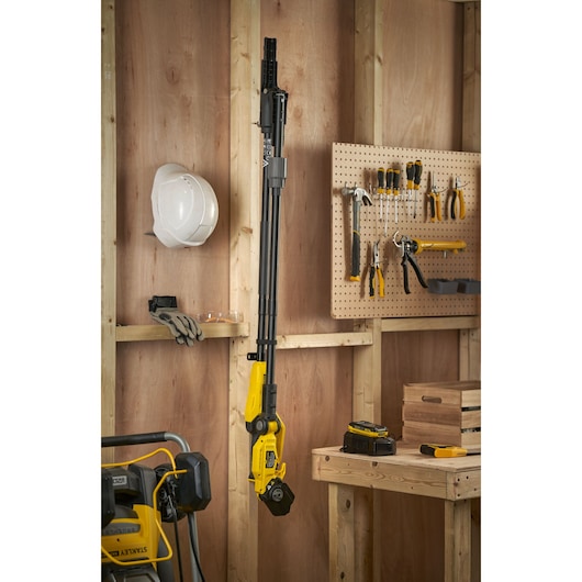 STANLEY SFMCPP632D1 pole saw hanging vertically in a workshop, surrounded by tools and safety gear.