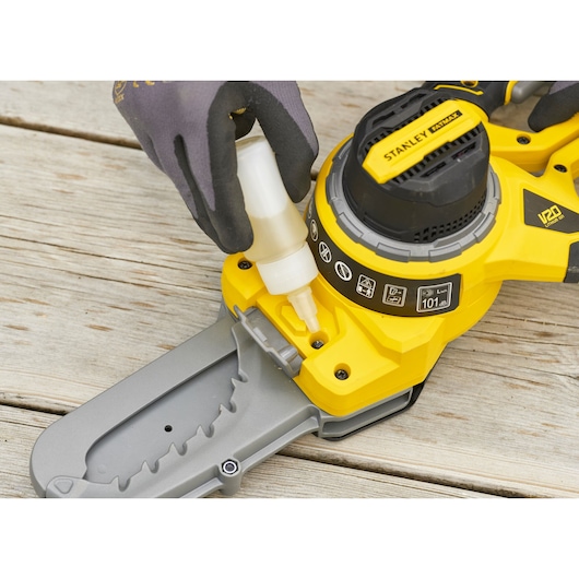 Photo of STANLEY SFMCPS515M1 chainsaw being oiled, close-up angle showing yellow and black tool.