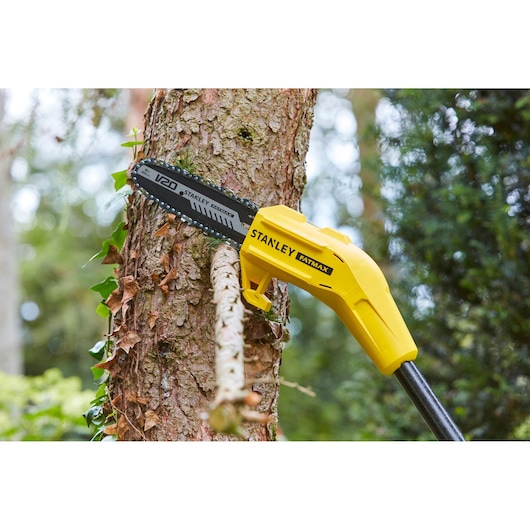 STANLEY SFMCPS620B pole saw cutting tree branch outdoors, yellow body with V20 blade visible.