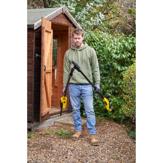 STANLEY SFMCPS720M1 pole saw held outdoors by person in garden near wooden shed.