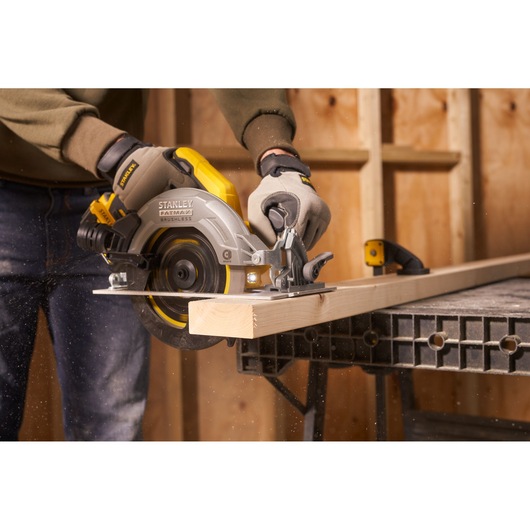 STANLEY SFMCS550M2K circular saw in use cutting wood in workshop, side view, yellow and silver design.
