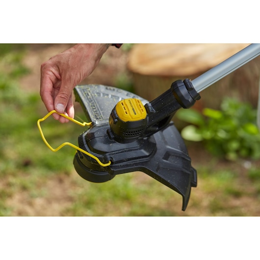 STANLEY SFMCST933B string trimmer close-up, yellow guard, user hand interacting outdoors.