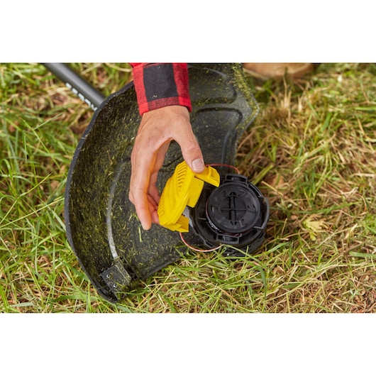 STANLEY SFMCSTB933B string trimmer close-up, hand attaching yellow cover to trimmer head on grass.