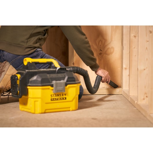 STANLEY SFMCV002B wet/dry vacuum in use, yellow and black, cleaning wooden floor corner.