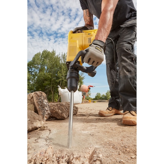 STANLEY SFMEH230K-QS demolition hammer in use breaking concrete outdoors, close-up on tool and worker’s hands.