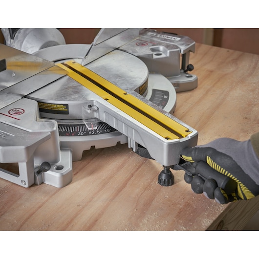 STANLEY SM1800 miter saw close-up, angled view, yellow rail, user adjusting handle, on wooden surface.